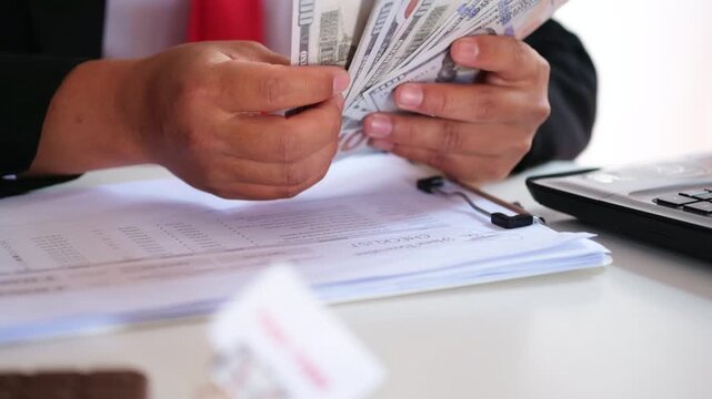 A sign reading "DEADLINE," clipped to a document, sits on a busy desk against a backdrop of an accountant counting dollars. The sign symbolizes a target that must be met before the deadline. Financial