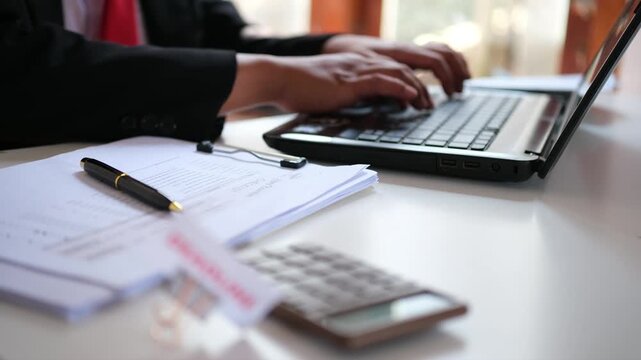A sign reading "DEADLINE," clipped to a document, sits on a cluttered desk against the backdrop of an accountant hurriedly typing on a laptop. The sign symbolizes a target that must be met before the 
