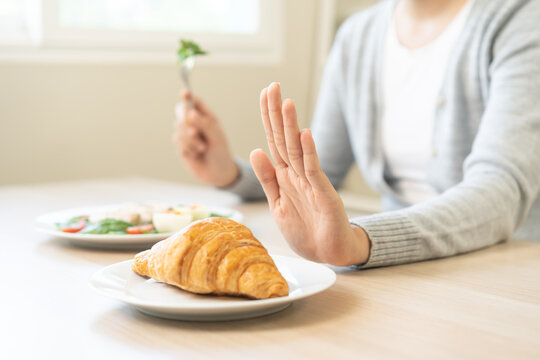 Ketogenic, Low carb, Intermittent Fasting diet woman push out, deny hand push out, deny butter croissant bread on plate, choose green vegetable salad, eat food for good healthy, getting weight loss.