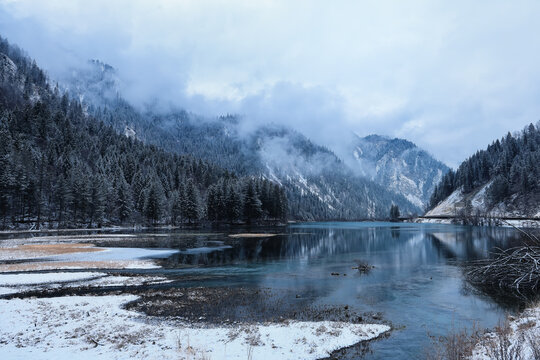 Winter landscape of Jiuzhaigou Valley, snowy mountains and partly frozen lake with pine forest in Sichuan, China