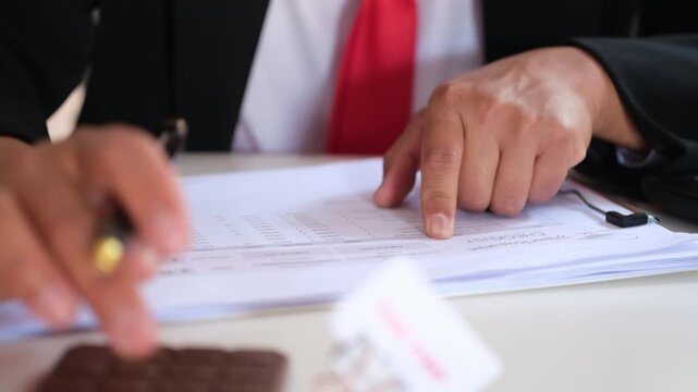A male accountant holds an invoice and calculates with a calculator. He analyzes expenses, bills, and finances at his desk.
