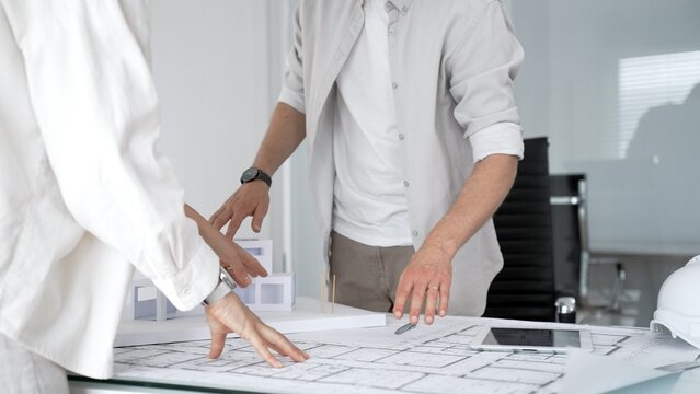 Architects and engineers collaborating on a new building project, examining architectural blueprints and a modern scale model for urban planning and development