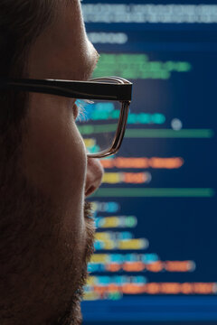 Rear view close up of a programmer in eyeglasses looking at screen with running programming code lines, working on machine learning or artificial intelligence development.