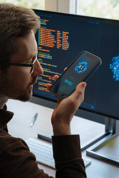 Over-the-shoulder view, of man holding smartphone, talking with AI chatbot app, asking questions, using artificial intelligence assistant for work and daily tasks on phone and computer. 