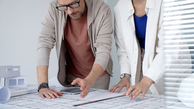 Architects and engineers collaborating on a building project, discussing blueprints and a house model while using a digital tablet for design planning and development