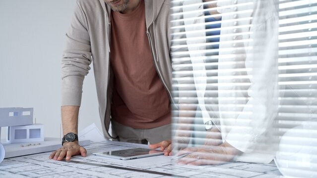 Architects and engineers collaborating on a building project, discussing blueprints and a house model while using a digital tablet for design planning and development