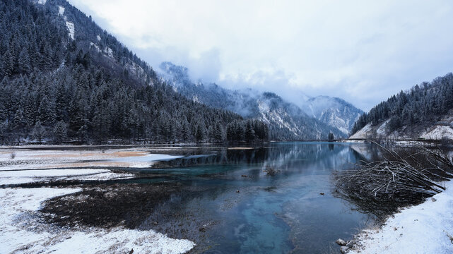 Winter landscape of Jiuzhaigou Valley, snowy mountains and partly frozen lake with pine forest in Sichuan, China