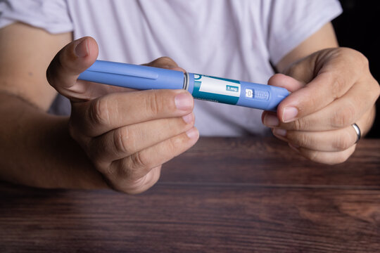 Person holding and adjusting a semaglutide subcutaneous injection pen for type 2 diabetes and obesity treatment at a dark oak wooden table.