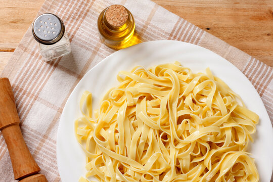 White ceramic plate containing freshly cooked fettuccine on a rustic table, accompanied by a textile napkin.