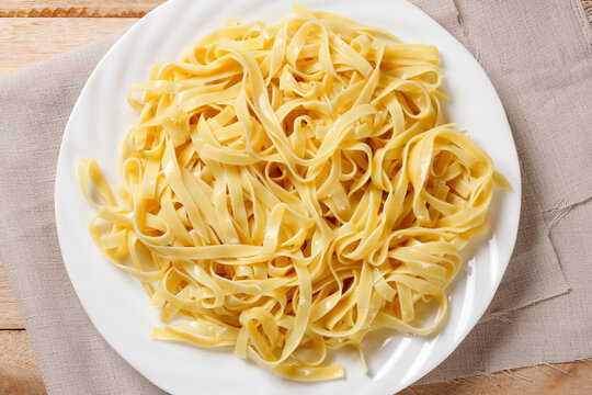 Cooked fresh fettuccine served on a white ceramic plate on a wooden table, accompanied by a cloth napkin in a cozy setting.