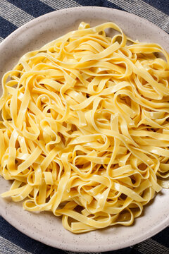 Cooked fresh fettuccine served on a rustic plate atop a blue striped cloth.