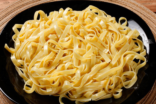 Golden cooked fettuccine served on a black plate on a wooden table, highlighting the pasta's tender texture and natural sheen.