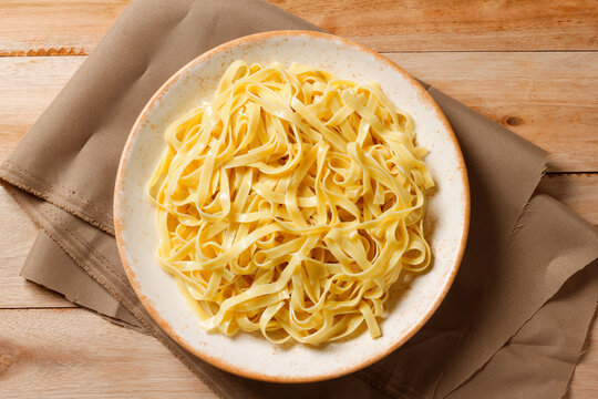 Cooked fresh fettuccine served on a rustic wooden plate with a cloth napkin.