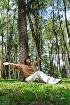 Vertical portrait image of a woman with opened arms sitting and relaxing in the park