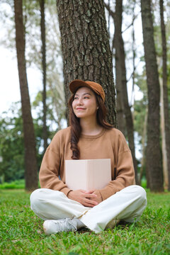 Vertical portrait image of a woman holding and reading a book while sitting in the park