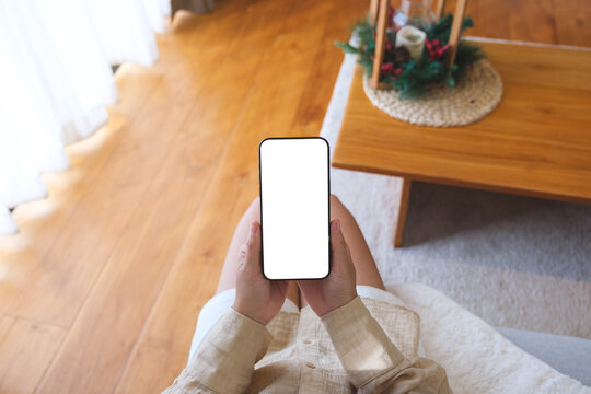 Top view mockup image of a woman holding and using mobile phone with blank desktop white screen at home
