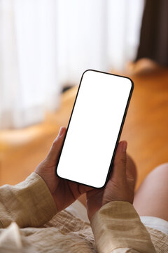 Vertical mockup image of a woman holding and using mobile phone with blank desktop white screen at home