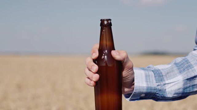 Man opens bottle of craft beer against backdrop of golden wheat field on sunny day, close-up shot of refreshing beverage.