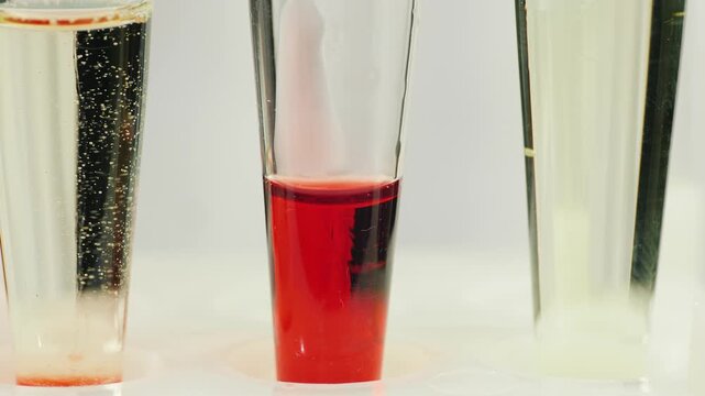 Close up of scientist using pipette to drip red liquid into laboratory test tubes for chemical analysis and research.