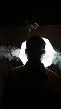 Atmospheric portrait of a man surrounded by thick smoke against a backlit studio light