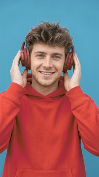 Young man in red hoodie smiling while listening to music with headphones