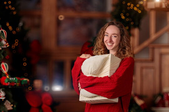 smiling young woman holding a wrapped holiday present in a cozy festive living room setting