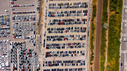Obraz premium High angle view of organized car rows in an outdoor distribution hub. Hundreds of passenger vehicles sit parked on a paved lot adjacent to railroad tracks.