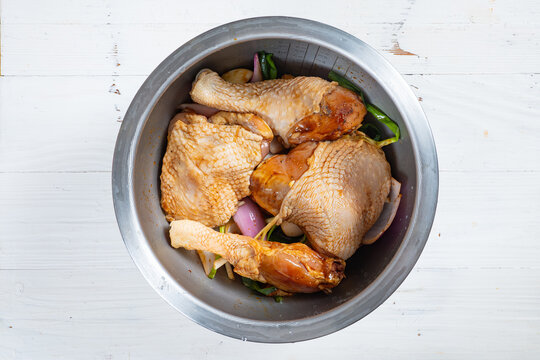Marinated raw chicken pieces mixed with vegetables in metal bowl