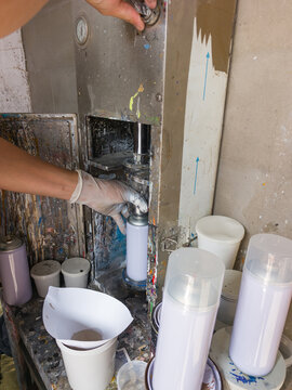 Worker operating aerosol can filling machine in paint workshop