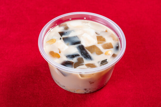 Milk dessert cup with grass jelly and assorted toppings on red