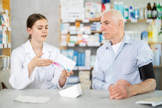 Female pharmacist helps elderly man measure blood pressure with tonometer