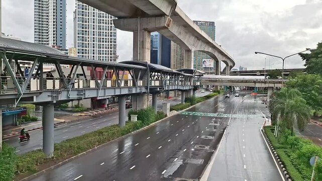 wet asphalt road and pedestrian skywalk bridge in bangkok city after rain with modern skyscraper buildings under cloudy overcast sky on September 27, 2026 in Bangkok, Thailand.