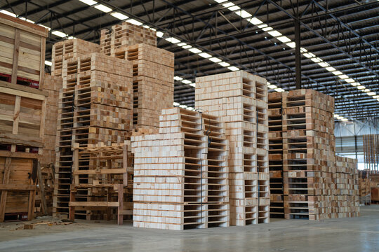 During pallet storage, a tall warehouse stack of wooden pallets stands in an unoccupied area beside wooden crates.
