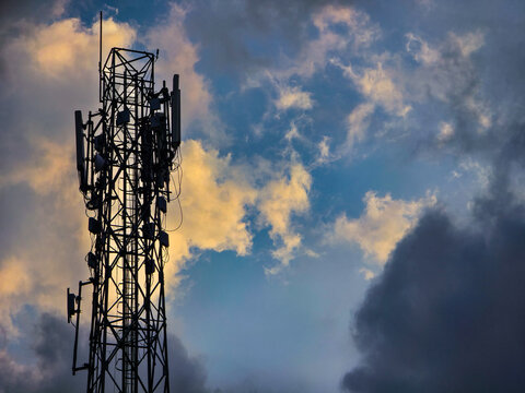 Silhouette of telecommunication tower against dramatic sky with golden sunset clouds. Perfect for 5G network, cellular technology, and wireless communication concepts.