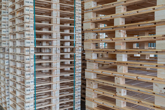 In pallet storage, a warehouse stack of wooden pallets stands among other stacks bound with visible green strapping.