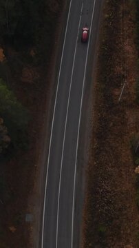 Drone footage looking straight down at a red car traveling along an empty asphalt road through dense autumn forest in the Ural Mountains, Russia, scenic travel concept