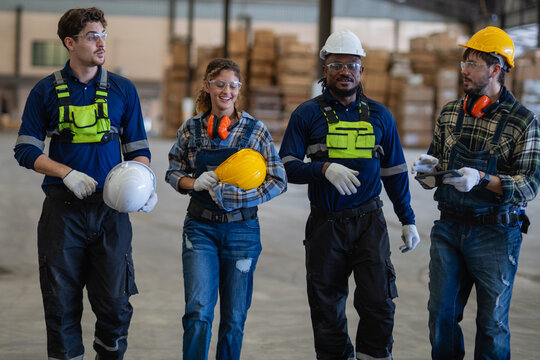 During factory teamwork discussions, four workers walk together for a team meeting, carrying a tablet past warehouse boxes.