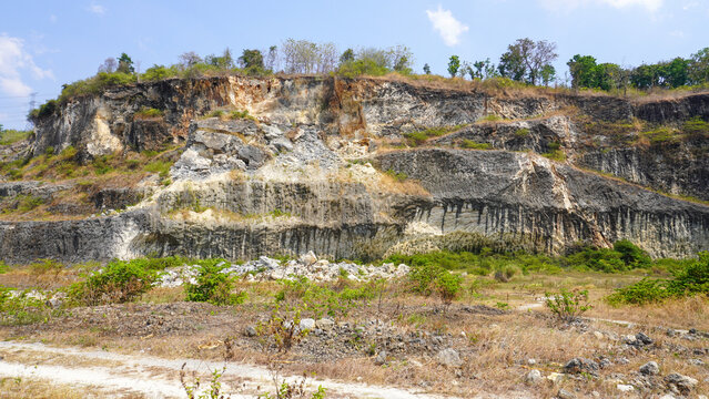Former limestone quarry site in Sukolilo, Pati, Central Java, Indonesia. Rugged cliff face of open-pit mine showing excavated white stone layers for cement and construction material production.