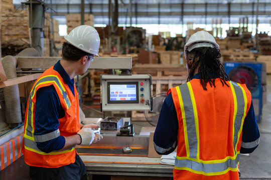Checking woodworking equipment for plywood, a carpenter and coworker stand at the edgebander control panel in a wood workshop.