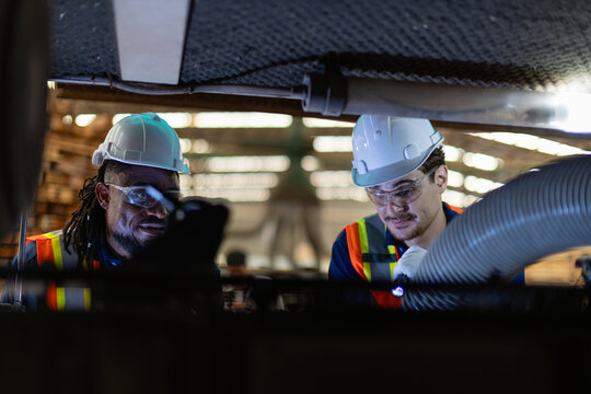 A technician performing machine maintenance uses a flashlight alongside another man while a third worker stands near the machinery.