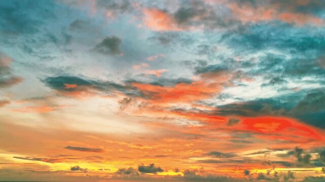 Spectacular vibrant sunset sky with colorful orange, red, and turquoise clouds moving at dusk. Majestic dramatic cloudscape at golden hour for background, weather forecast, or travel project.