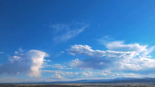 Panoramic aerial view of a vibrant blue sky filled with moving white cumulus clouds over distant hills.