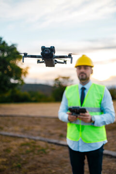 Drone flying above a man in a safety vest and hard hat in an outdoor setting