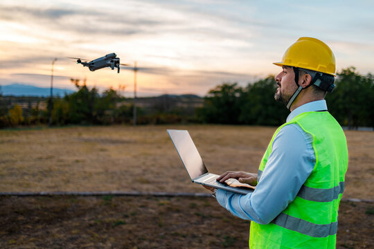 Worker operates drone while standing in open field during sunset