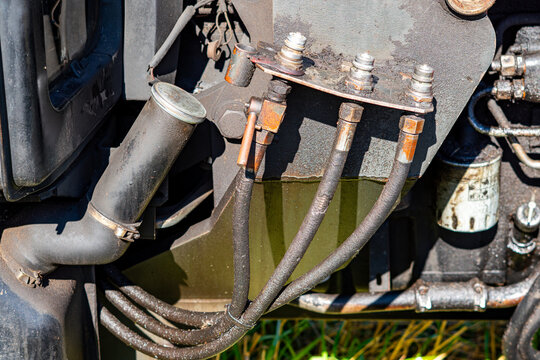 Close-up photo of an old, dirty agricultural machinery hydraulic system featuring metal quick couplers, flexible hoses, and an oil filler pipe, with visible signs of wear in direct sunlight.   