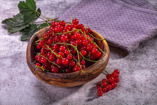 Fresh red currants in wooden bowl on textured surface with green leaves and purple cloth