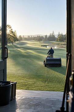 Groundskeeper operating a turf aerator on a golf course