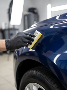 Technician hand applying ceramic coating on dark blue vehicle body paint.