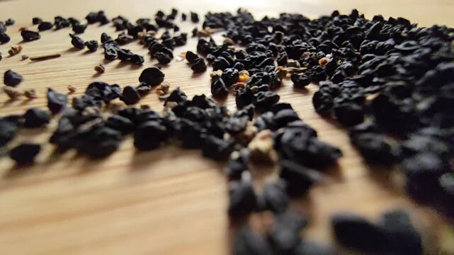 Macro close-up video of organic leek seeds scattered across a wooden surface, highlighting agricultural harvesting, gardening concepts, and healthy plant-based ingredients in a natural setting.   