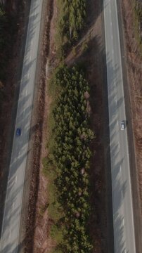 Top down aerial footage of a divided highway cutting through dense pine forest with a few cars driving, shot in the Ural region, Russia, travel and transport concept